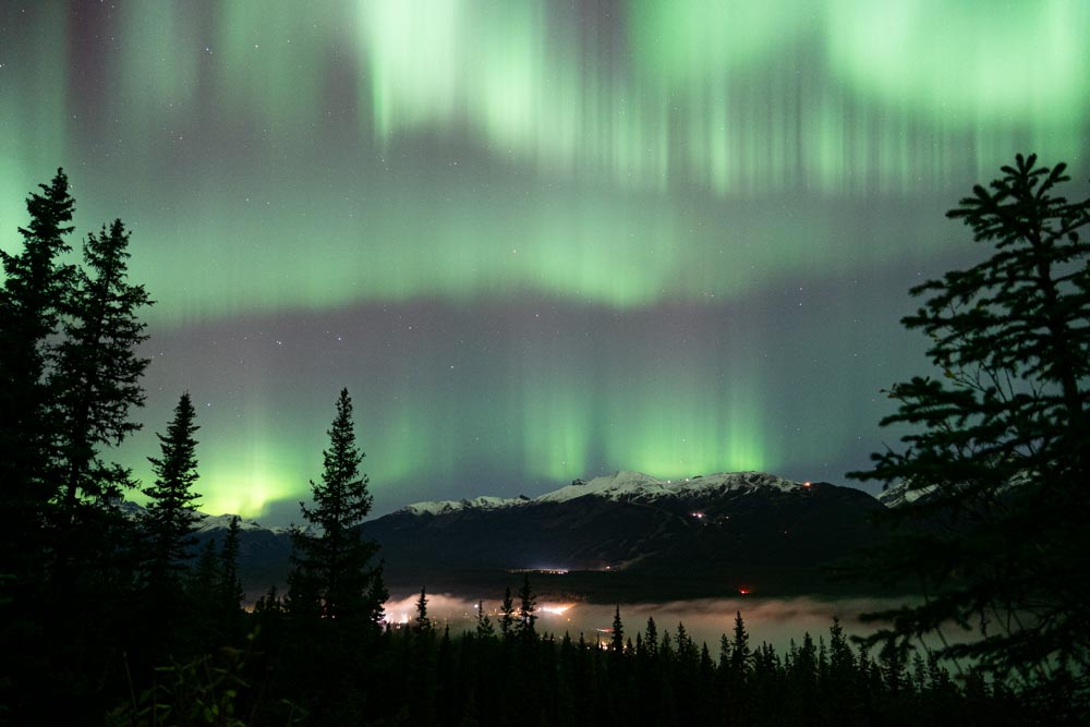Green aurora curtains glow above the Lake Louise Ski Resort and alpine ridge at night.