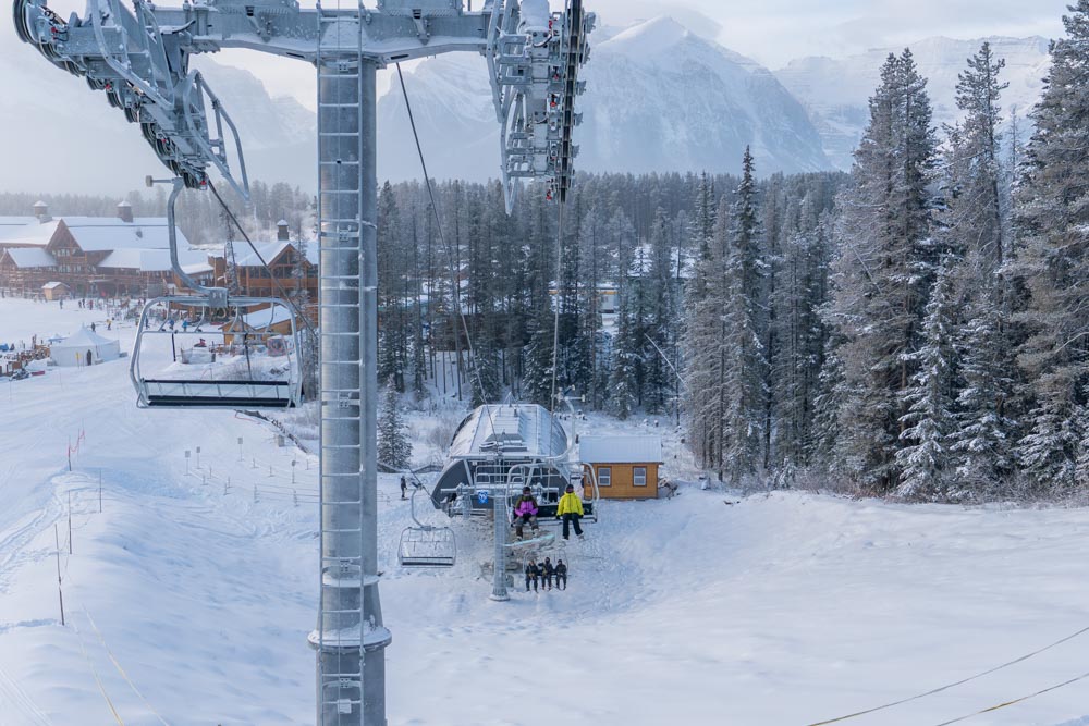 Original: Chairlift approaches a base‑area station beside frosted trees and lodge buildings on a cold winter morning.
