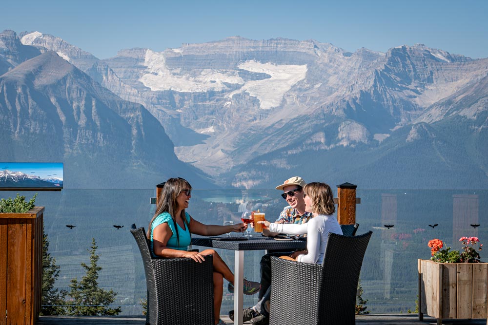 Original: Friends toast drinks on the Whitehorn Bistro patio with Lake Louise and glaciers in the background.
