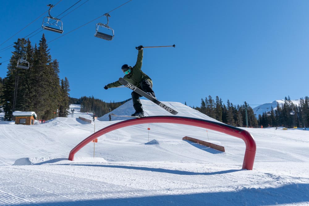 Freestyle skier slides a red rainbow tube in the terrain park on a bluebird day.